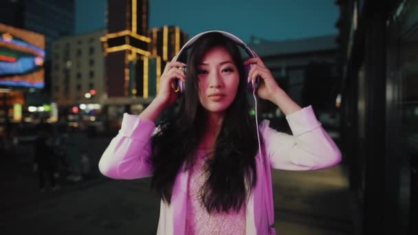 Азиатка надевает наушники в ночном городе — стоковое видео