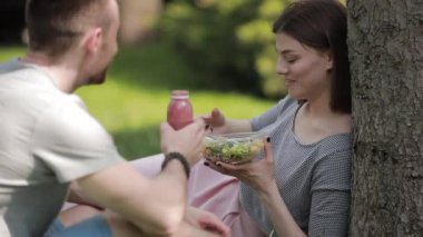 Genç vejetaryen çift parkta oturmuş salata yiyor ve smoothie içiyor.