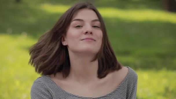 Портрет улыбающейся счастливой молодой женщины в парке, выбрасывающей волосы — стоковое видео