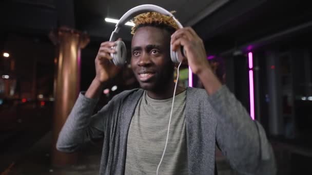 Mutlu Afrikalı Amerikalı adam gece yeraltı yerde kulaklık giyiyor — Stok video