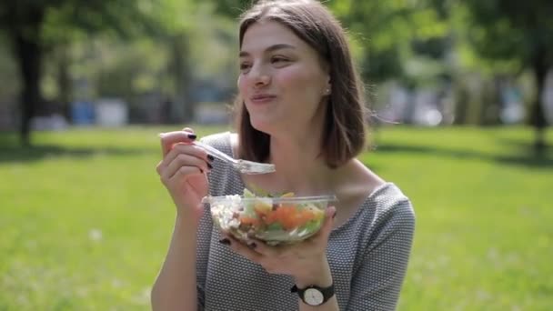 Щаслива жінка насолоджується свіжим салатом, сидячи в літньому парку — стокове відео