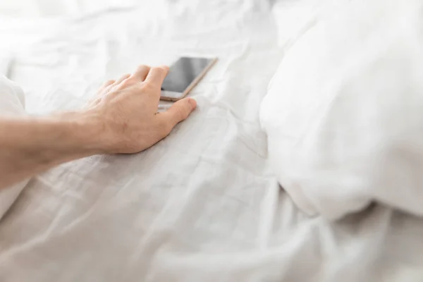 Mano maschile raggiunge lo smartphone subito dopo il risveglio a letto — Foto Stock