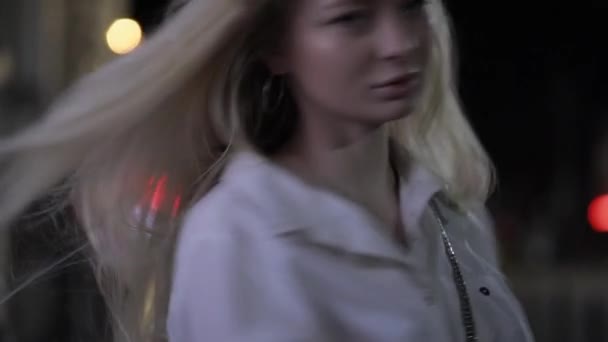 Досить блондинка модель позує торкаючись довгого волосся в нічному місті — стокове відео