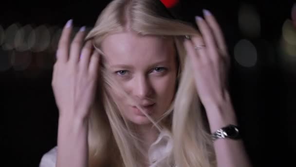 Сексуальна блондинка позує торкаючись довгого волосся в нічному місті — стокове відео
