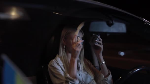 Женщина-водитель носит наушники в машине в ночном городе — стоковое видео