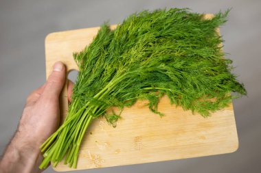 Bir erkek elinde bir kesme tahtasında dereotu