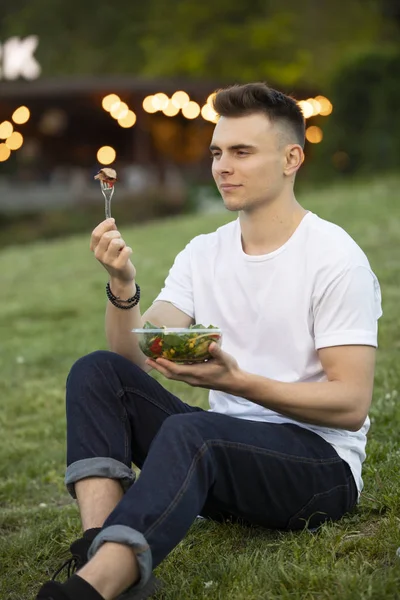 Man eating fresh salad at summer, holding fork with meat
