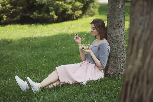 Mulher comendo salada fresca sentado no parque de verão — Fotografia de Stock