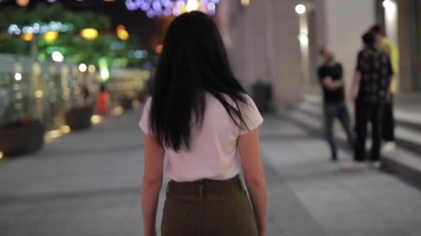Mujer caminando en la ciudad nocturna mirando hacia atrás — Vídeos de Stock
