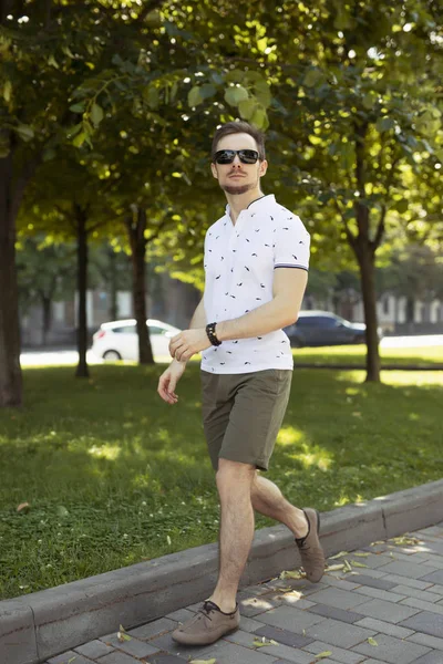 Модний чоловік в поло і шорти, що йдуть на літній алеї — стокове фото