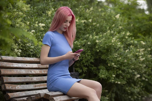 Epätavallinen nainen vaaleanpunaiset hiukset älypuhelimella penkillä — kuvapankkivalokuva