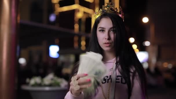 Rich girl in crown like queen blowing hair with money at night city — Stock Video