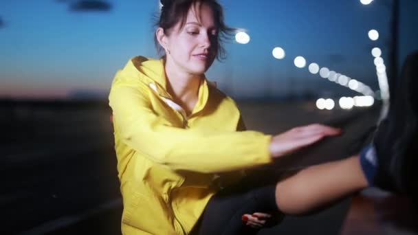 Спортивная женщина растягивает ногу в ночном городе — стоковое видео