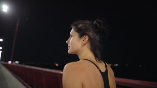 Женщина едет по ночному мосту, вид сзади — стоковое видео