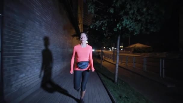 Deportiva corriendo por la noche calle de la ciudad con auriculares — Vídeo de stock