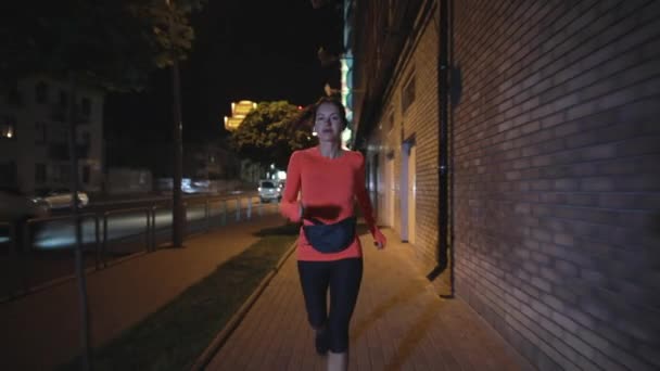 Deportiva corriendo por la noche calle de la ciudad con auriculares — Vídeos de Stock