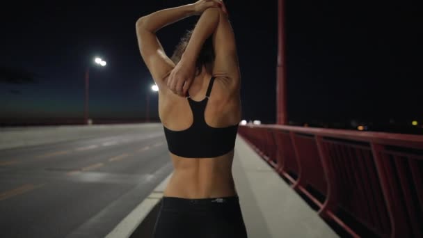 Спортивная женщина греется в ночном городе перед пробежкой — стоковое видео