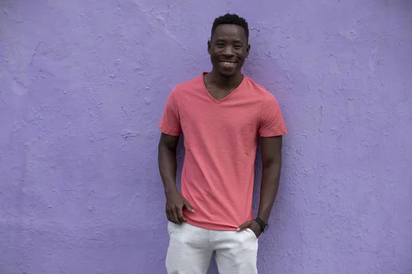 Modelo de hombre afroamericano sonriente posando en una camiseta de coral viva vacía en la pared violeta — Foto de Stock