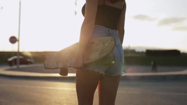 Woman skateboarder carries her skateboard in hands at sunset — Stock Video