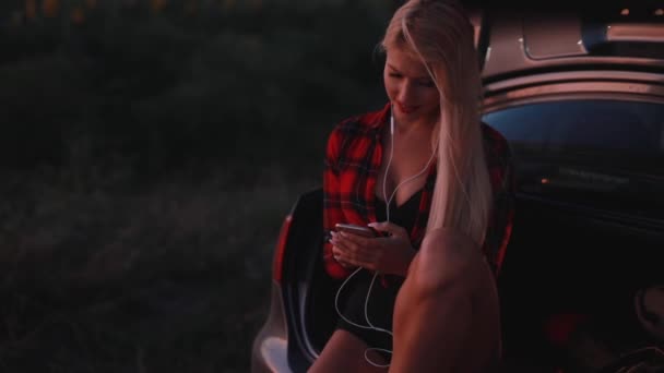 Сексуальная женщина слушает музыку в наушниках, сидя на машине — стоковое видео