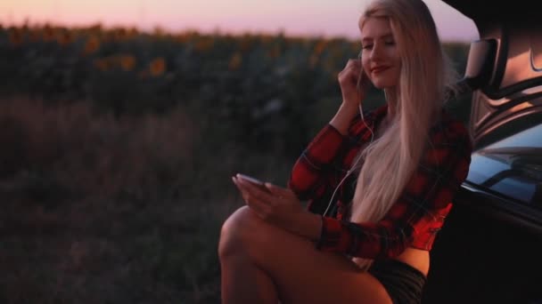 Mujer sexy escuchando música en auriculares sentados en el coche — Vídeos de Stock