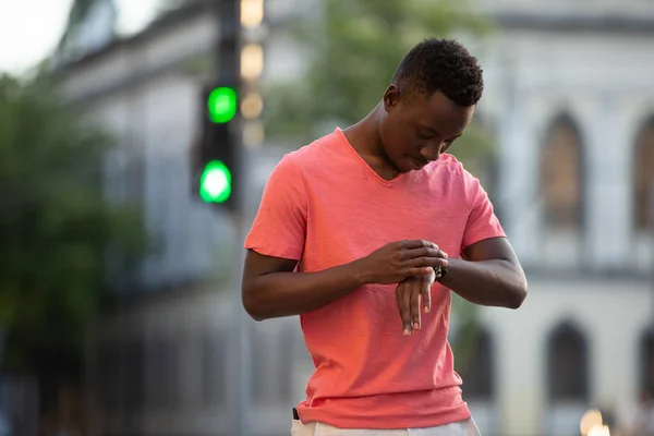 Афроамериканець людина в живих коралових футболки дивлячись час в місті — стокове фото