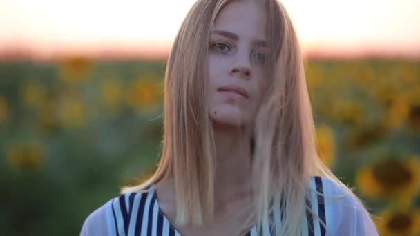Κορίτσι στο πεδίο στο ηλιοβασίλεμα κοιτάζοντας την κάμερα, άνεμος φυσάει τα μαλλιά — Αρχείο Βίντεο