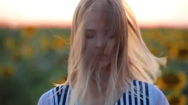 Дівчина в полі на заході сонця дивиться на камеру, вітер дме волосся — стокове відео