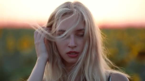 Mujer en el campo al atardecer mirando a la cámara, el viento sopla su cabello — Vídeo de stock