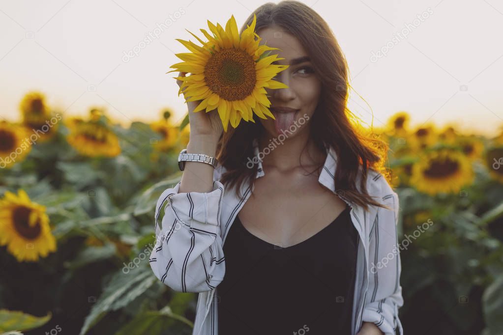Funny woman in sunflower field showing tongue