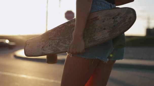 Vrouw skateboarder draagt haar skateboard in handen bij zonsondergang — Stockvideo