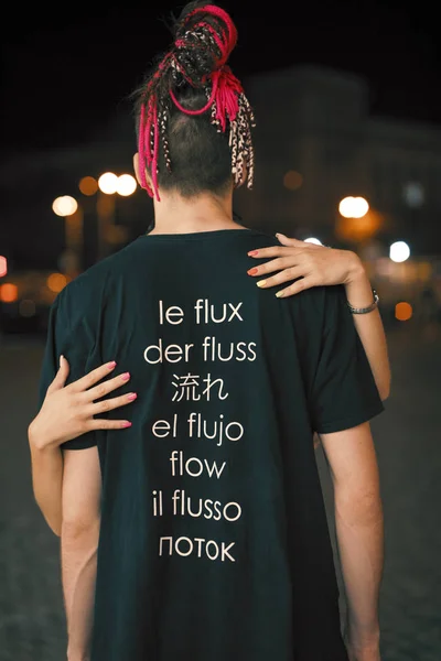 Mies t-paidassa virtaava sana eri kielillä yökaupungissa, peruutusnäkymä — kuvapankkivalokuva