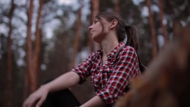 Kvinnan sitter på trädstammen i skogen och kopplar av och ser sig omkring — Stockvideo
