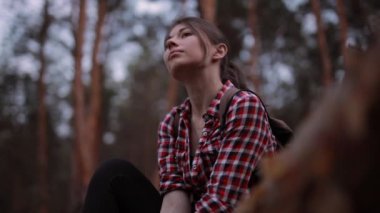 Ormandaki ağaç gövdesinde oturan ve etrafa bakan bir kadın.