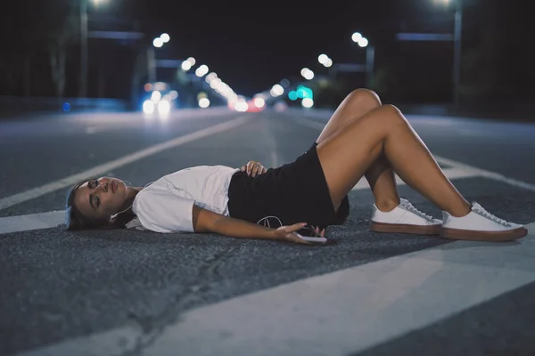 Žena v poupatech, která ležela na noční cestě a poslouchala hudbu v sluchátek — Stock fotografie