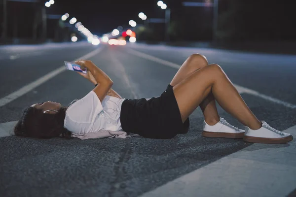 Woman in earbuds lying on night road listening music making selfie — Stock Photo, Image