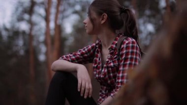 Ormandaki ağaç gövdesinde oturan ve etrafa bakan bir kadın.