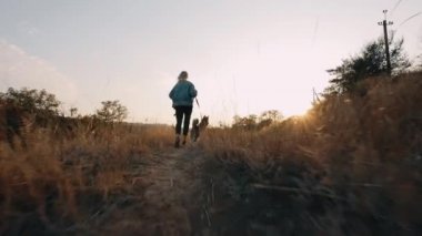 Gün batımında köpekle koşan bir kadın. Dertsiz tasasız evcil hayvanla geçirilen yaz zamanı.