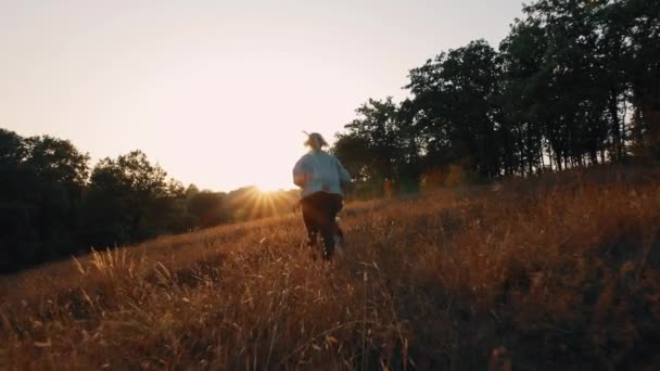 Žena běhající se psem v přírodě při západu slunce. Carefree užívat letní čas s domácím mazlíčkem. — Stock video