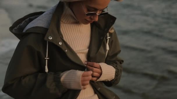 Mujer con estilo en gafas de sol usan sudadera con capucha de pie en el río — Vídeos de Stock