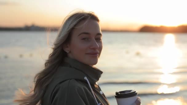 Lycklig kvinna njuter av solnedgången och vända ansiktet ser på mig står nära floden — Stockvideo