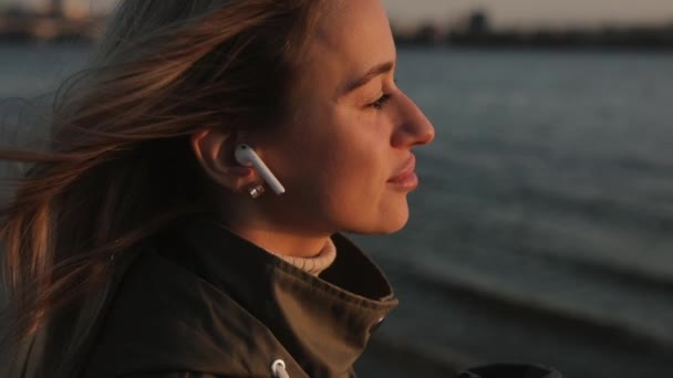 Mujer escuchando música en auriculares parados cerca del río — Vídeo de stock