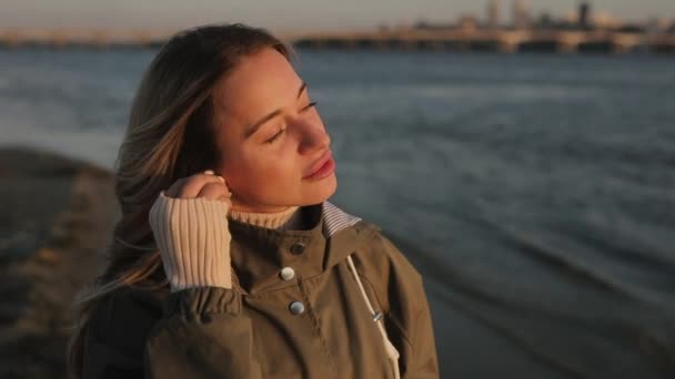Жінка слухає музику в навушниках, що стоять біля річки — стокове відео