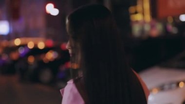 Şık Asyalı bir kadın gece şehirde yürürken yüzünü ve arkasını döner.
