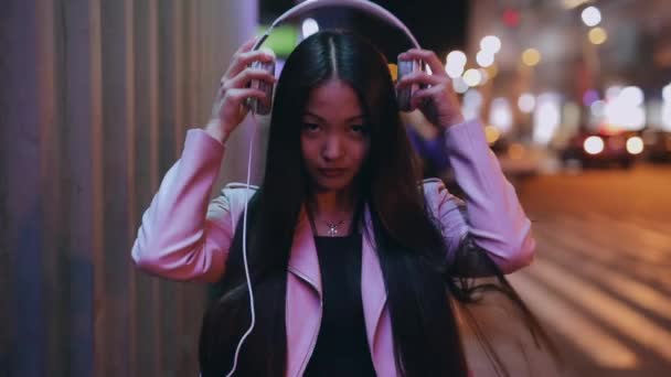 Asiática mujer pone en auriculares caminando en la noche de la ciudad — Vídeos de Stock