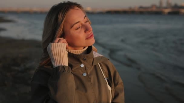 Женщина слушает музыку в наушниках, стоящих возле реки — стоковое видео