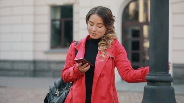 Женщина отправляет сообщение на смартфоне и смотрит в камеру — стоковое видео