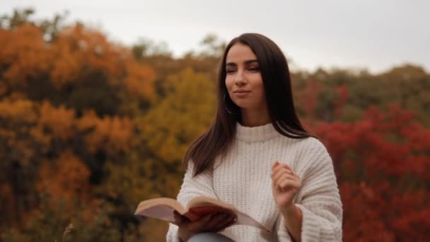 Woman reading book sitting in the autumn forest leaning head on hand — Stock Video