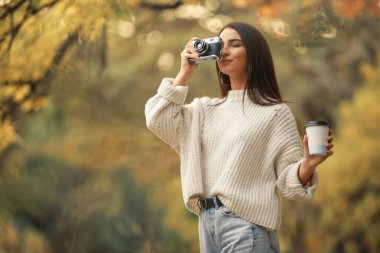 Kadın fotoğrafçı sonbahar ormanında yürürken fotoğraf çekmek