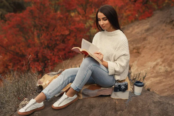 Жінка читає книгу, сидячи в осінньому лісі — стокове фото